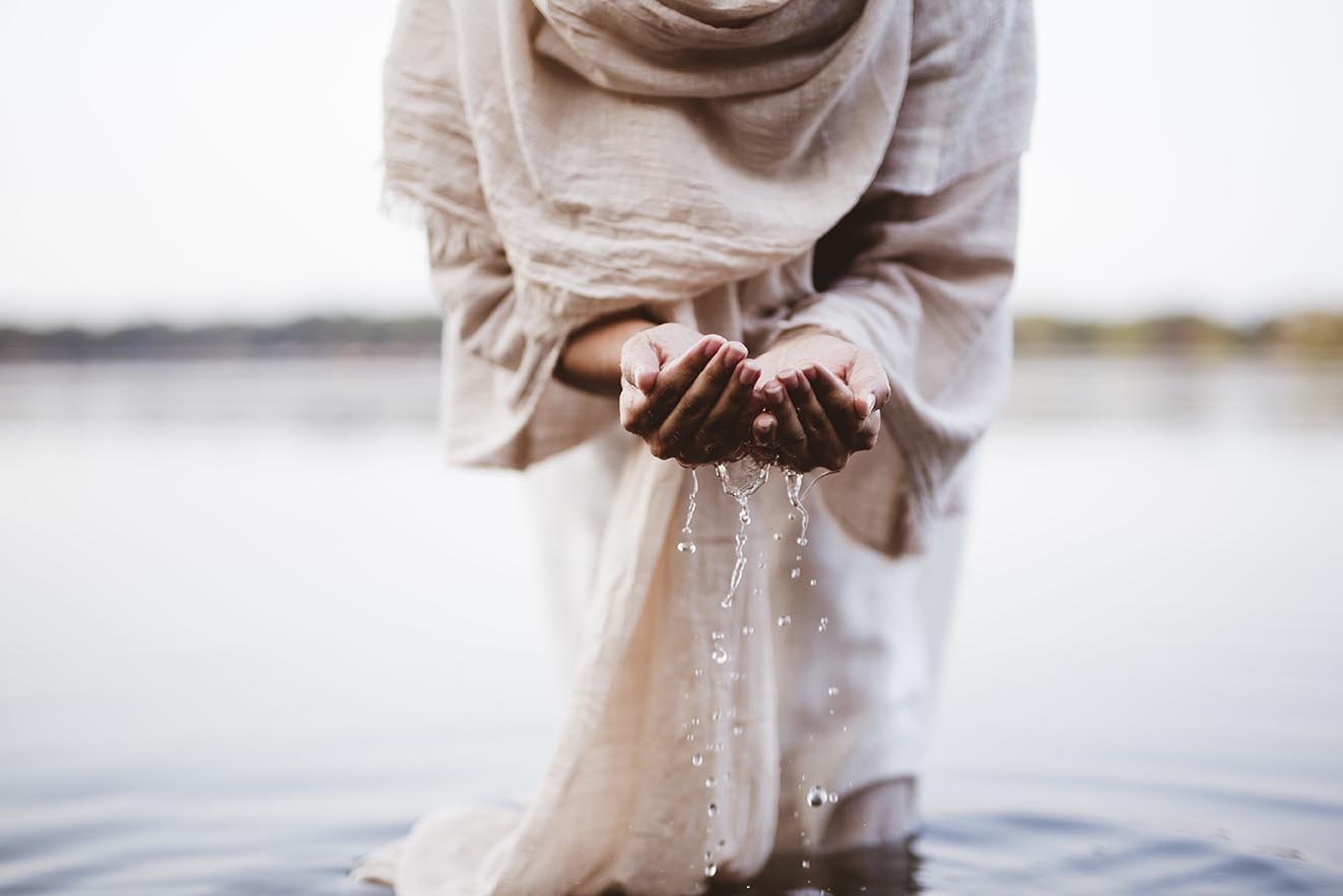 A closeup shot of a female wearing a biblical robe holding water with her palms
